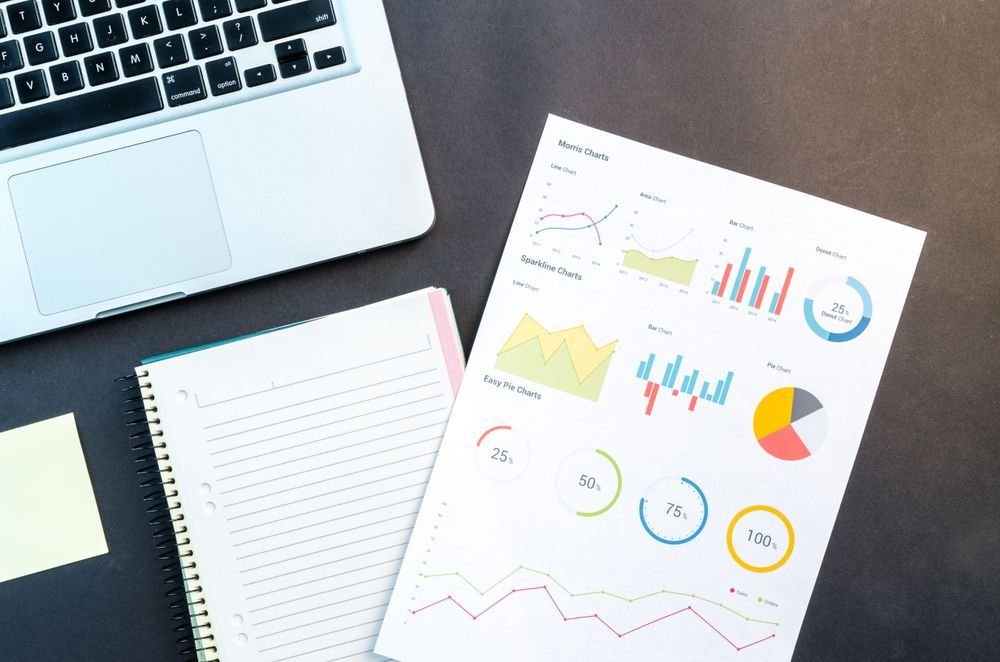 Notebook, laptop and printed charts on a desk, representing research-led investing