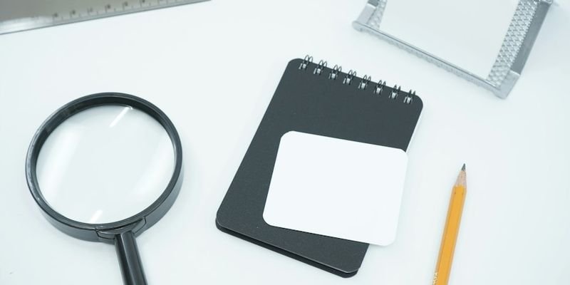 Magnifying glass on a desk beside a notebook, representing tracing old company and folio records